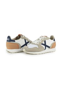 Baskets alliant cuir blanc, suède beige et accents bleu marine, avec un dos texturé et des détails en mesh blanc sur l'orteil.