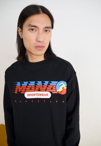 Sudadera negra con un estampado gráfico multicolor con líneas horizontales, nombre de la marca y logo en colores vibrantes. Textura de tela suave.