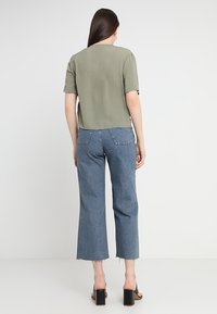 Grön kortärmad topp med en lös passform, matchad med blå beskurna jeans med fransade fållar och hög midja. Svarta klacksandaler synliga.