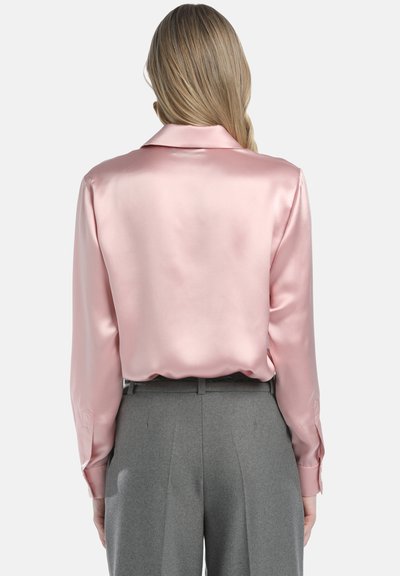 Helles rosa Satinbluse mit Kragen und langen Ärmeln, kombiniert mit grauen, taillierten Hosen mit Bund und gefaltetem Frontbereich.