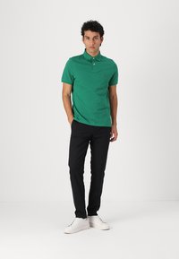 Grøn bomulds polo-shirt med krave, korte ærmer og et lille logo. Parret med sorte bukser og hvide sneakers.