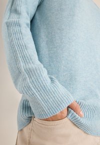 Jasnoniebieski sweter z dzianiny z prążkowanymi mankietami i dołem. Miękka tekstura, dopasowany krój. Pasuje do chinosów, pokazując szczegóły kieszeni.