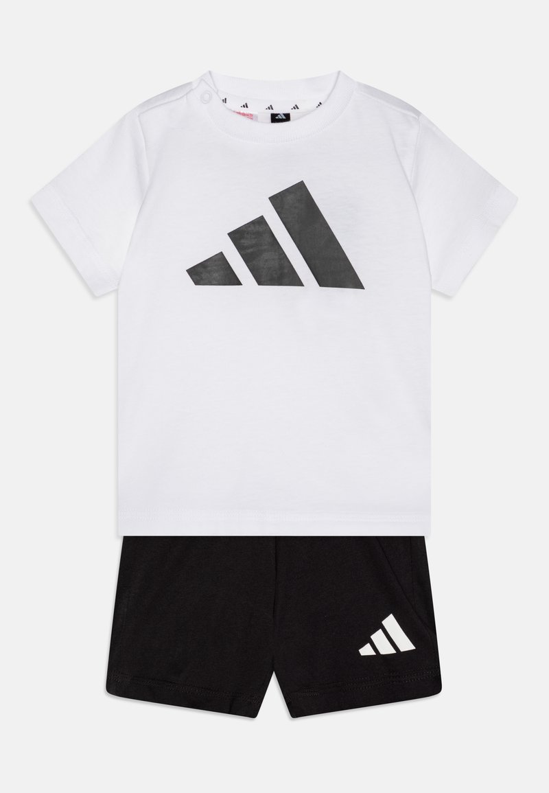 Biela bavlnená tričko s veľkým čiernym logom Adidas, v kombinácii s čiernymi šortkami s malým bielym logom na nohavici.