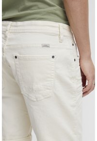 Hvite jeans med teksturert finish, som har to baklommer, en liten logo-lapp og metallnagler på lommestipene.