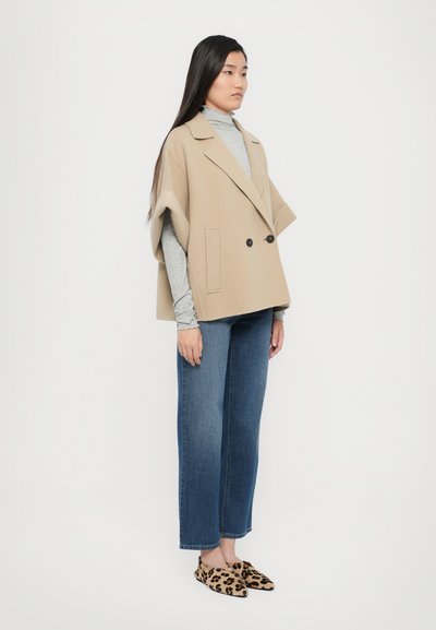 Beige wool-blend double-breasted cape, gray turtleneck, blue straight-leg jeans, and leopard-print slip-on shoes. Smooth texture, relaxed fit.