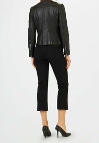 Veste en cuir noir à coupe ajustée, zips sur les manches, associée à un jean noir court et des chaussures noires à talons. Lignes épurées et style minimaliste.