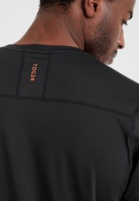 Black athletic shirt with a smooth texture, featuring orange branding at the neckline and flatlock seams for comfort and fit.