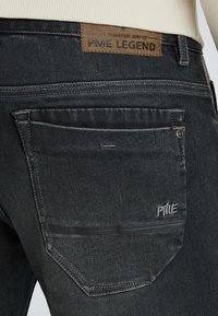 Zadná vrecko tmavosivých džínsoch s nášivkou PME Legend na páse a vyšitým logom PME na vrecku.