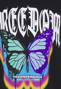 Svart t-shirt med en stor, färgglad fjärilsgrafik med blå och lila vingar, droppande målarfärgs-effekter och texten "FRIHET" ovanför.