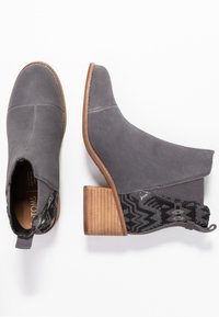Botines de ante gris con un panel elástico negro texturizado y un tacón de bloque de madera. Cuentan con una punta redondeada y detalles de costura mínimos.
