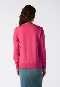 Felpa fucsia con maniche lunghe e polsini a coste, caratterizzata da un collo rotondo e una texture liscia e morbida. Indossata sopra una gonna di denim.