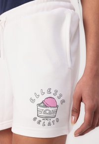 Pantaloni corti bianchi realizzati in tessuto morbido, con una grafica ispirata al gelato dai colori pastello e la scritta "ELLLESSE GELATO". Inclusi taschini laterali.