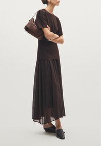 Brown two-piece outfit featuring a fitted top and flowing maxi skirt. Paired with a dark handbag and open-toed black shoes.