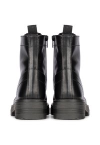 Bottines en cuir noir avec une texture lisse, dotées d'une fermeture éclair sur le côté et d'une languette, ainsi qu'une semelle en caoutchouc épaisse pour une meilleure adhérence.