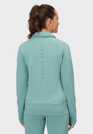 Light mint green sweatshirt with a funnel neck, featuring a vertical "VENICE BEACH" text on the back. Smooth fabric and fitted design.