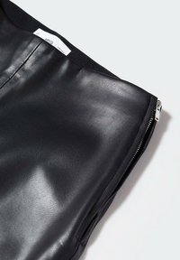Gros plan d’une jupe en cuir noire avec une fermeture éclair visible sur le côté et une ceinture élastique avec une étiquette de taille intérieure.