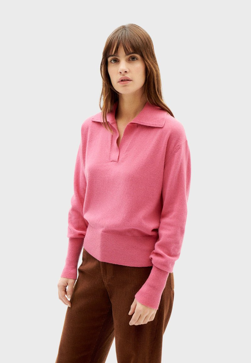 Roze gebreide trui met een kraag, lange mouwen en geribde manchetten en zoom. Glad textuur, losse snit, gecombineerd met bruine corduroy broek.