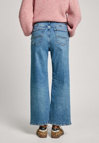 Jeans de pierna ancha en azul claro con un diseño clásico de cinco bolsillos, que presentan detalles de costura sutiles. Llevados con zapatos de estampado animal.