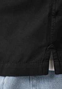 Tessuto di cotone nero con una superficie liscia, con aperture laterali all'orlo e abbinato a denim azzurro chiaro.