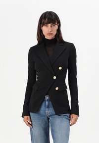 Zwarte dubbelbreasted blazer met gouden knopen, getailleerde pasvorm en twee voorzakken, gecombineerd met lichtblauwe high-waisted spijkerbroeken.