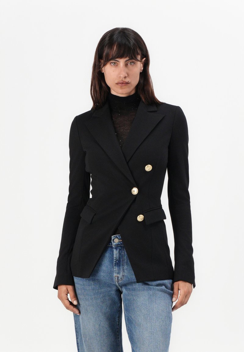 Zwarte dubbelbreasted blazer met gouden knopen, getailleerde pasvorm en twee voorzakken, gecombineerd met lichtblauwe high-waisted spijkerbroeken.