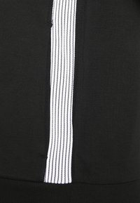 Felpa nera con una riga verticale bianca sul lato, realizzata in tessuto morbido con una finitura testurizzata.