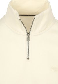 Cream-colored fleece pullover with a high collar, featuring a front zip closure and subtle embroidered logo on the lower right.