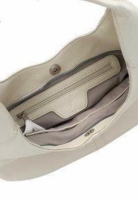 Interno della borsa a mano in pelle crema con finitura testurizzata, dotato di una tasca con zip, una tasca a scomparsa e foderato in tessuto liscio.