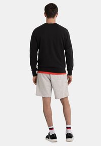 Black sweatshirt with a round neckline, gray shorts, and black sneakers. Features ribbed cuffs and waist, layered with a red shirt underneath.