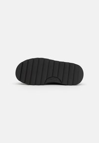 Suela de zapato de goma negra con una textura acanalada, forma redondeada y un logo sutil. Talla 37 indicada en la parte inferior.