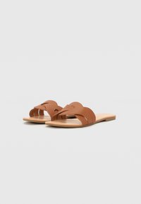 Bruine leren slide-sandalen met een uitsnijdontwerp en een platte tan rubberen zool. Heeft gebogen banden over de voet voor een comfortabele pasvorm.