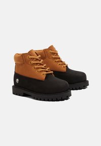 Botas de tobillo de cuero marrón y negro con cuello acolchado, cordones y suela de goma texturizada que presenta un logotipo distintivo en el costado.