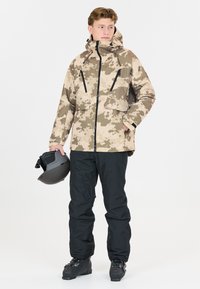 Miestenska lyžiarska bunda v hnedo-beige camouflage vzore, s vysokým golierom, dvoma prednými vreckami a čiernymi zipsami. Čierne lyžiarske nohavice a topánky.