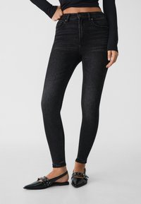 Jeans ajustados de tiro alto en un material de denim, con un leve desvanecimiento. Combinados con zapatos de tacón con punta negra y detalles.