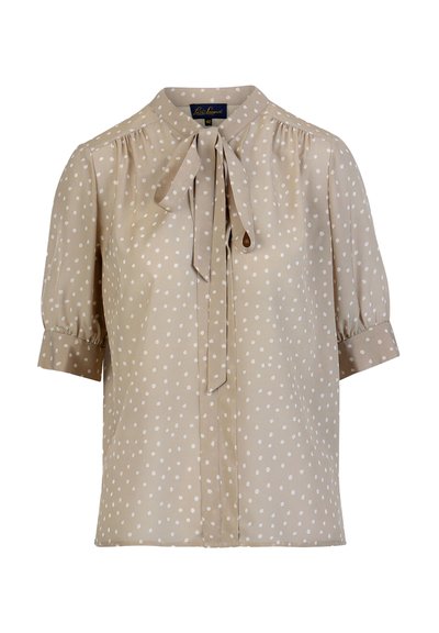 Bež bluza z belimi pikami, kratkimi napihnjenimi rokavi in detajlom zavezave okoli vratu. Izdelana je iz gladkega, lahkega materiala z udobnim ohlapnim krojem.