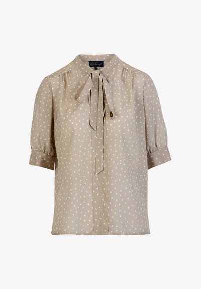 Bež bluza z belimi pikami, kratkimi napihnjenimi rokavi in detajlom zavezave okoli vratu. Izdelana je iz gladkega, lahkega materiala z udobnim ohlapnim krojem.