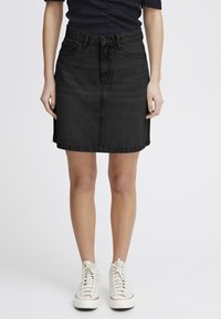 Jupe en denim noir à coupe droite, longueur mi-cuisse, cinq poches, passants de ceinture et détails de couture discrets ; portée avec des baskets blanches.