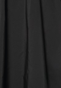Tissu noir avec des plis doux et une texture lisse, suspendu verticalement avec des ombres subtiles.