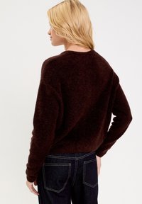 Maglione a maglia marrone scuro con una vestibilità ampia, collo a giro, e maniche lunghe, abbinato a jeans in denim scuro, visto da dietro.