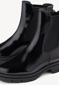 Paire de bottines Chelsea en cuir verni noir avec des panneaux latéraux élastiques et des semelles épaisses en caoutchouc sur fond blanc.
