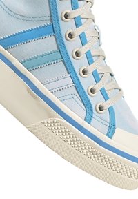 Vaaleansininen kangaskenkä, jossa on valkoisia ja vaaleansinisiä yksityiskohtia. Kenkässä on teksturoitu pohja, metalliset nauholevyt ja kontrastiväriset ompeluyksityiskohdat.