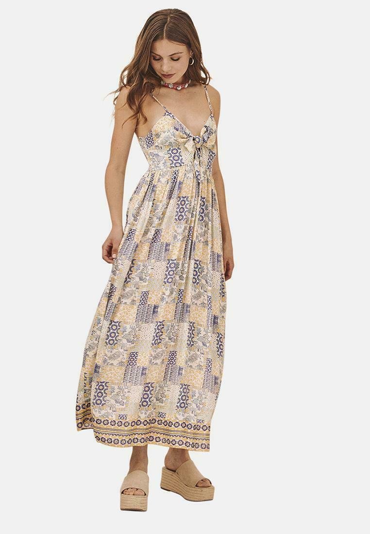 Vestido maxi en amarillo claro con patrones geométricos en azul y crema. Presenta un lazo en la parte delantera, tirantes finos y una silueta fluida.