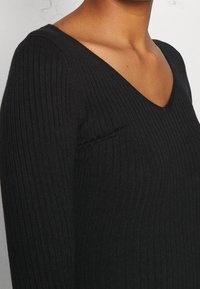 Maglione nero a coste con scollatura a V. Presenta un design aderente, tessuto testurizzato e maniche lunghe, che mette in risalto una finitura liscia.