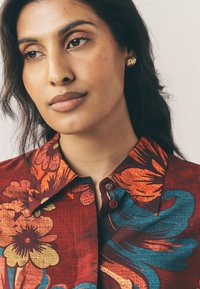 Red floral-patterned shirt with blue accents and a collar, featuring a button closure. Smooth texture with a vibrant, bold design.