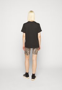 Svart bomullst-shirt med korta ärmar kombinerad med metallic slangmönstrade cykelshorts. Svarta sneakers fulländar outfiten.