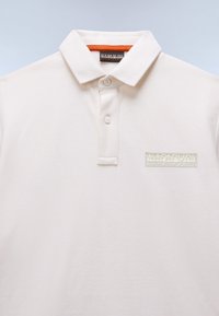 Πόλο μπλούζα σε εκρού χρώμα, κατασκευασμένη από βαμβάκι με υφή. Διαθέτει γιακά, δύο κουμπιά και ένα ανοιχτοπράσινο λογότυπο στο αριστερό μέρος του στήθους.