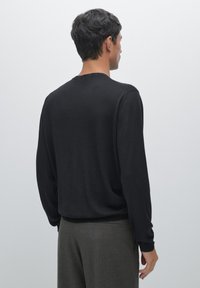 Maglione nero a maniche lunghe con scollatura a girocollo, realizzato in tessuto morbido e leggero, con vestibilità rilassata e polsini a costine, abbinato a pantaloni grigi a righe.