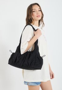 Svart stoffhåndveske med samlet tekstur og justerbare snor detaljer, med en bred stropp og et mykt, plisséert design.