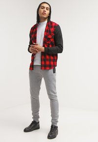 Camisa de franela de cuadros en rojo y negro con capucha negra, combinada con pantalones jogger grises y zapatillas negras. Cuenta con dos bolsillos en el pecho.