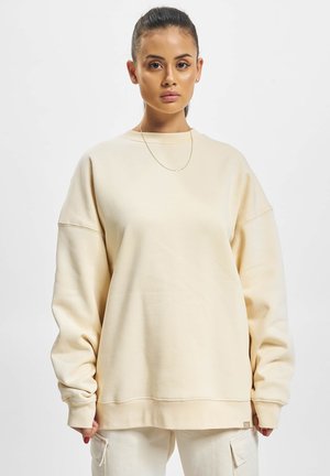 Beige overdimensjonert genser med lange ermer og rund hals. Myk stoff med en glatt tekstur og ribbede mansjetter og nederkant.